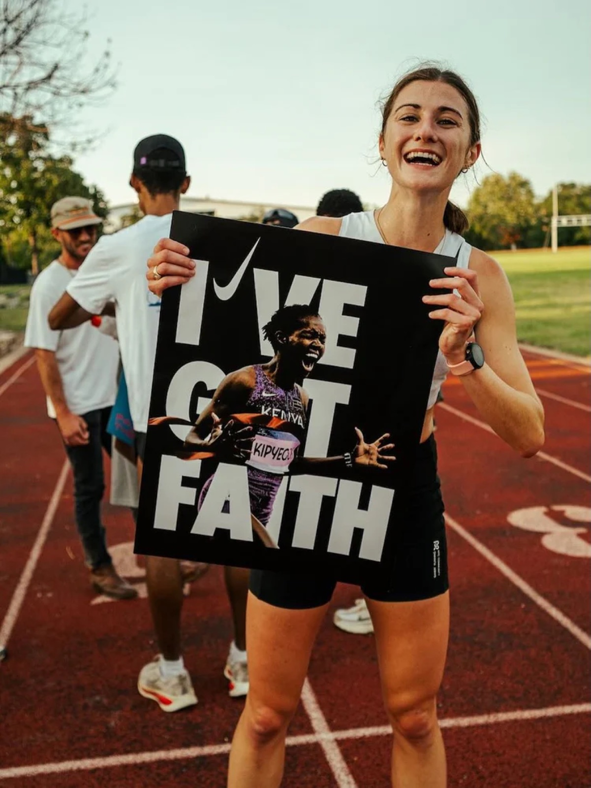 Runner at a track watch party holding the black I’VE GOT FAITH Breaking4 poster of Faith Kipyegon